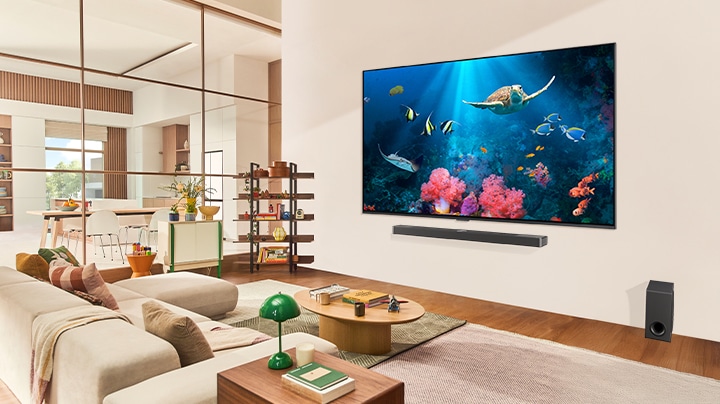 Rodzina w salonie z bardzo du?ym LG TV zamontowanym na ?cianie przedstawiaj?cym scen? oceanu z koralowcami i ?ó?wiem na ekranie.