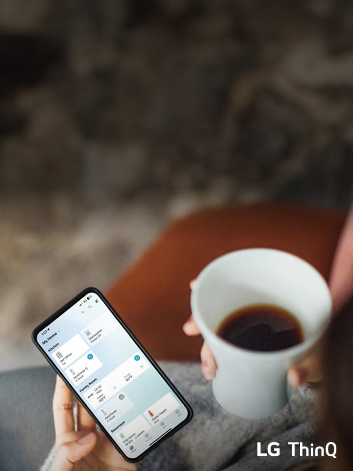 Osoba trzymaj?ca smartfon z aplikacj? LG ThinQ, pij?c kaw?.