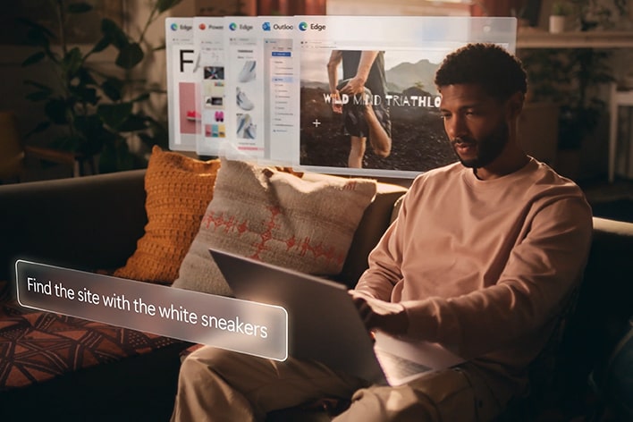 Ein Mann sitzt auf einer Couch und benutzt einen Laptop. Auf einer virtuellen Benutzeroberfl?che wird der Text ?Finde die Seite mit den wei?en Turnschuhen“ angezeigt und über dem Laptop-Bildschirm schweben mehrere Browser-Registerkarten.
