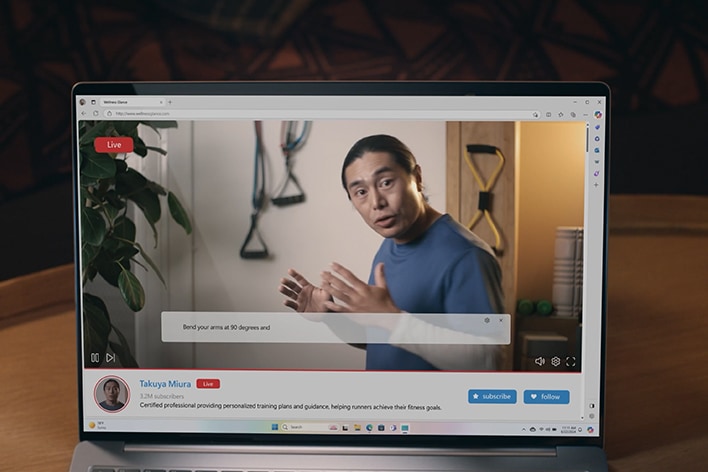 Auf dem Laptop-Bildschirm wird eine Live-übertragung angezeigt, die einen sprechenden Mann zeigt. W?hrend er spricht, erscheinen am unteren Bildschirmrand Untertitel mit automatischen übersetzungen.