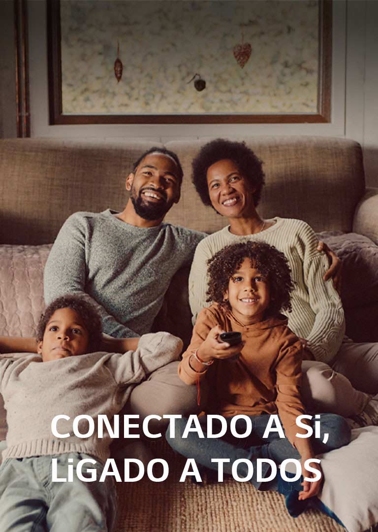 Uma imagem de uma família de quatro pessoas sentadas no ch?o em frente a um sofá castanho acolhedor, olhando em frente e rindo enquanto vêem televis?o. As palavras “Syncs to you, open to all” (Sincroniza-se consigo, aberto a todos) sobrep?em-se à imagem num tipo de letra branco. 