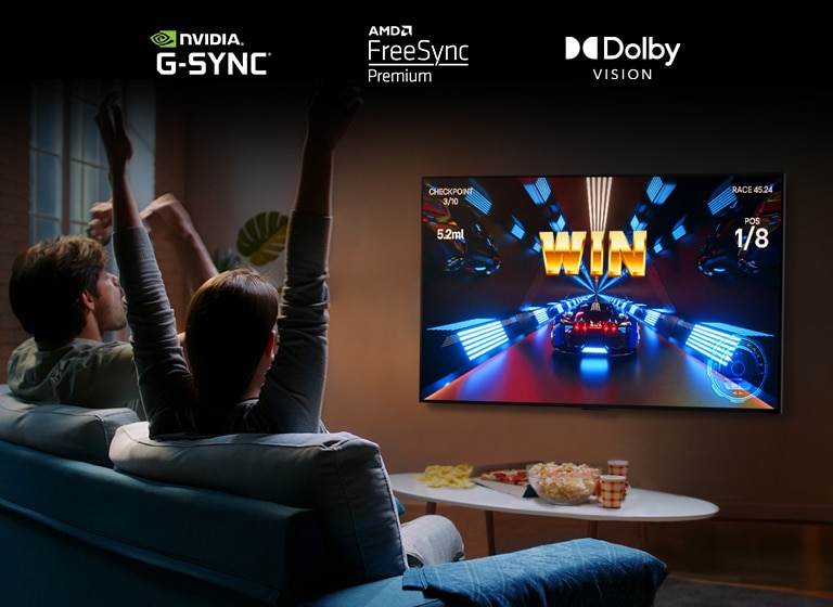 Tv? personer sitter p? en soffa i ett vardagsrum, de har en kontroll och spelar ett bilspel p? LG OLED G2.