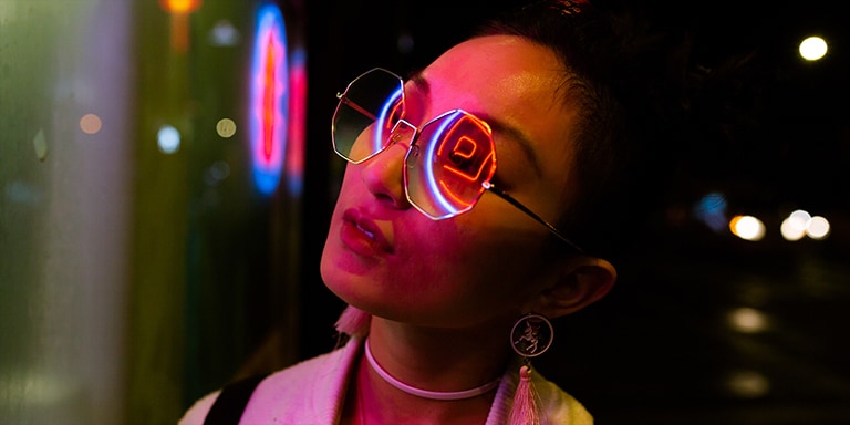 En n?rbild av en kvinna som b?r solglas?gon och neonljus som reflekteras p? henne.
