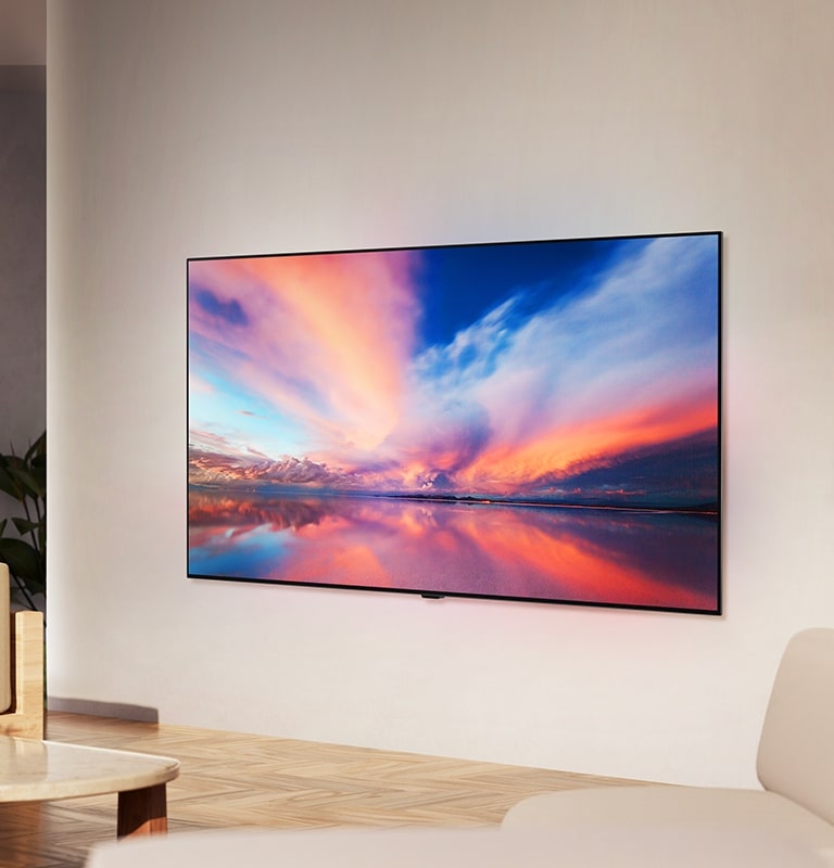 LG OLED TV, OLED B4 p? v?ggen i ett neutralt vardagsrum som visar ett f?rgstarkt foto av en solnedg?ng ?ver havet.