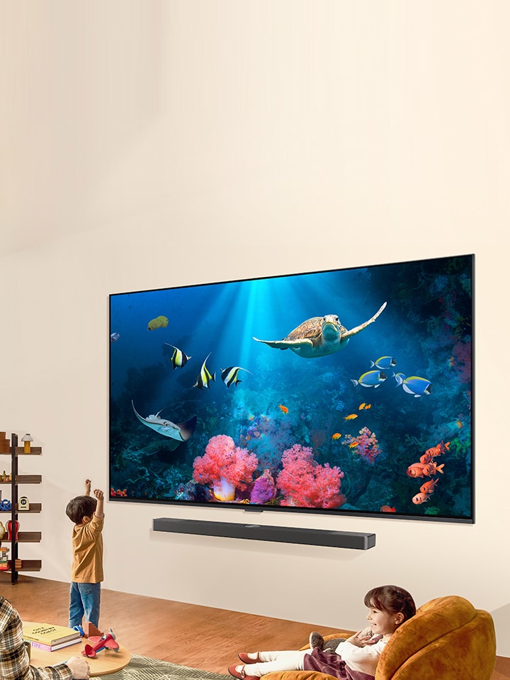 G?rüntüde, bir aile parlak ve do?al bir ya?am alan?na yerle?tirilen LG Soundbar’l? LG QNED TV’de parlak bir su sahnesini seyrediyor.