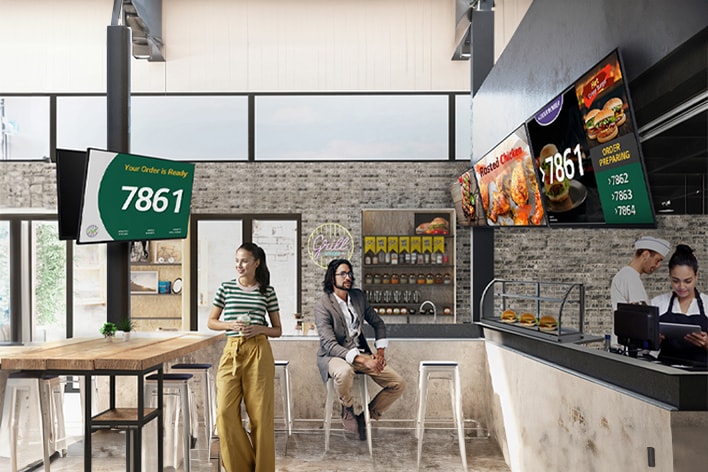 圖片突出顯示快餐店 (QSR) 中的多臺顯示器，顯示著排隊號碼和產品圖片等內容。	