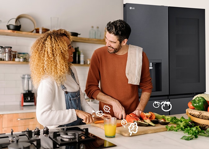 Le couple cuisine en souriant devant le réfrigérateur.
