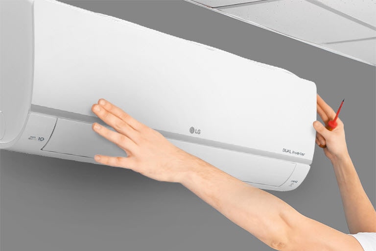 Person adjusting a white LG Dual Inverter air conditioner mounted high on a grey wall near a ceiling with grid panels.