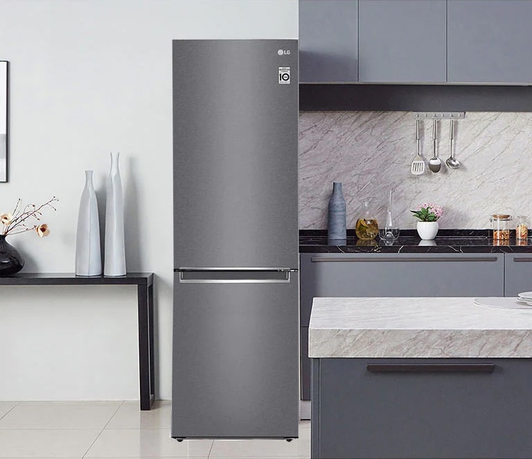 Grey LG refrigerator in a modern kitchen with grey cabinets, marble countertops, vases, and utensils on the wall.