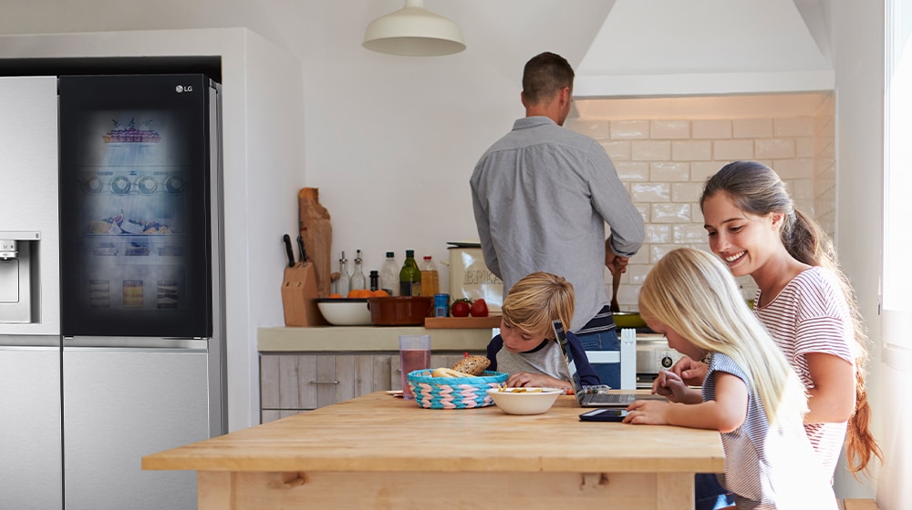 Modern kitchen with LG fridge, family engaged in activities, cooking and studying at wooden dining table.