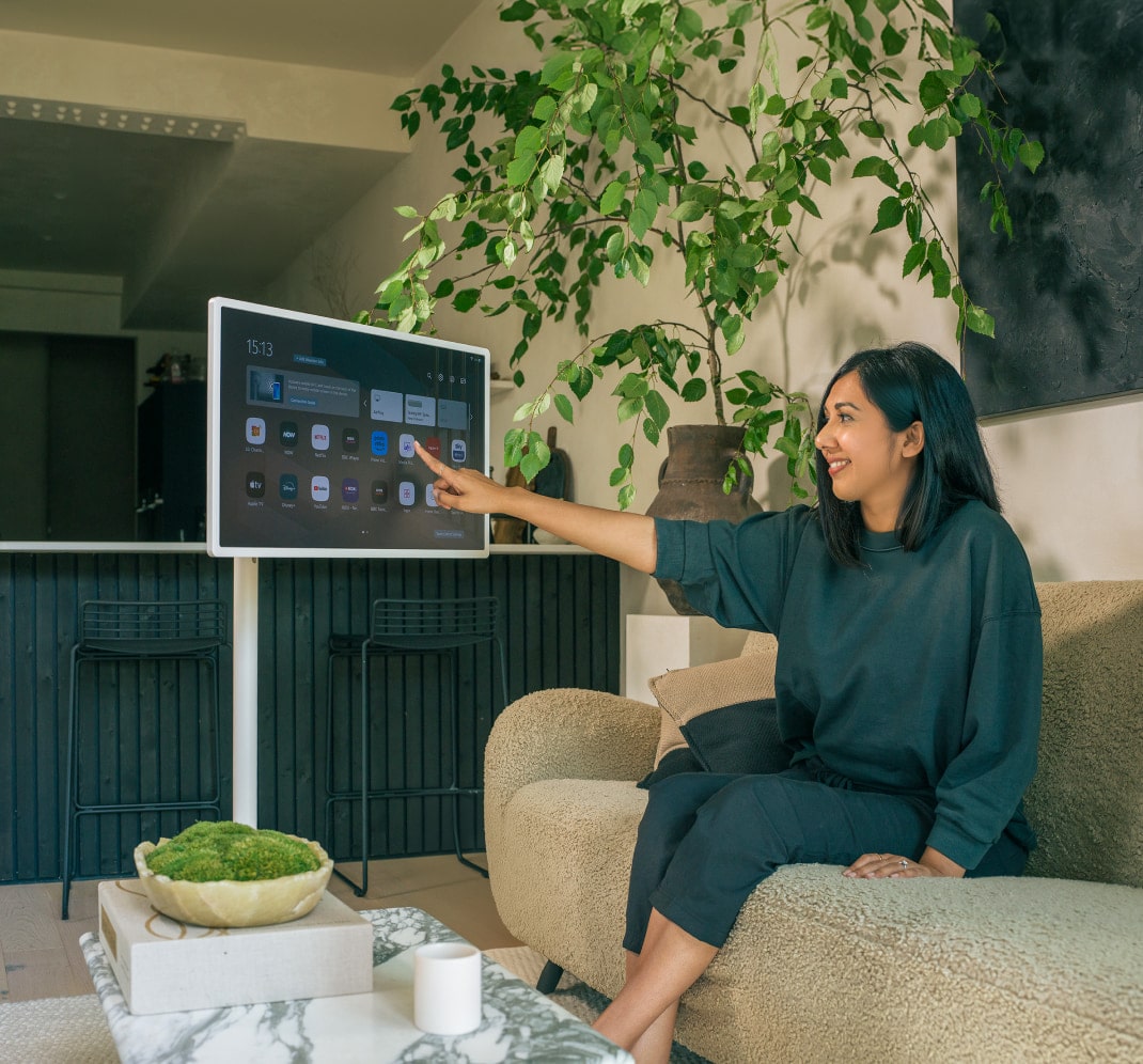 Lisa Mistry is sitting on her living room sofa, smiling as she touches the screen of the LG StandbyME.