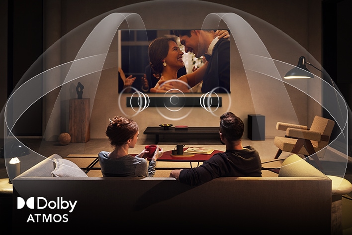 Phòng khách ?m cúng, l? m? sáng có c?p ??i ?ang xem phim trên LG TV v?i LG Soundbar. Dolby Atmos l?p ??y kh?ng gian v?i am thanh vòm t? m?i h??ng. Logo Dolby Atmos ? góc d??i cùng.
