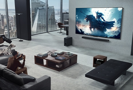 Phòng khách v?i m?t ng??i ?ang ch?i trò ch?i ?i?n t? trên TV LG True Wireless và LG Soundbar treo t??ng. Anh c?m m?t b? ?i?u khi?n trong tay, nh?ng máy ch?i game kh?ng d? ?? nhìn th?y ngay l?p t?c. C?ng kh?ng có day nào có th? nhìn th?y. H?p k?t n?i kh?ng day ???c gi?u kín, h?u nh? kh?ng nhìn th?y bên d??i bàn ph?.