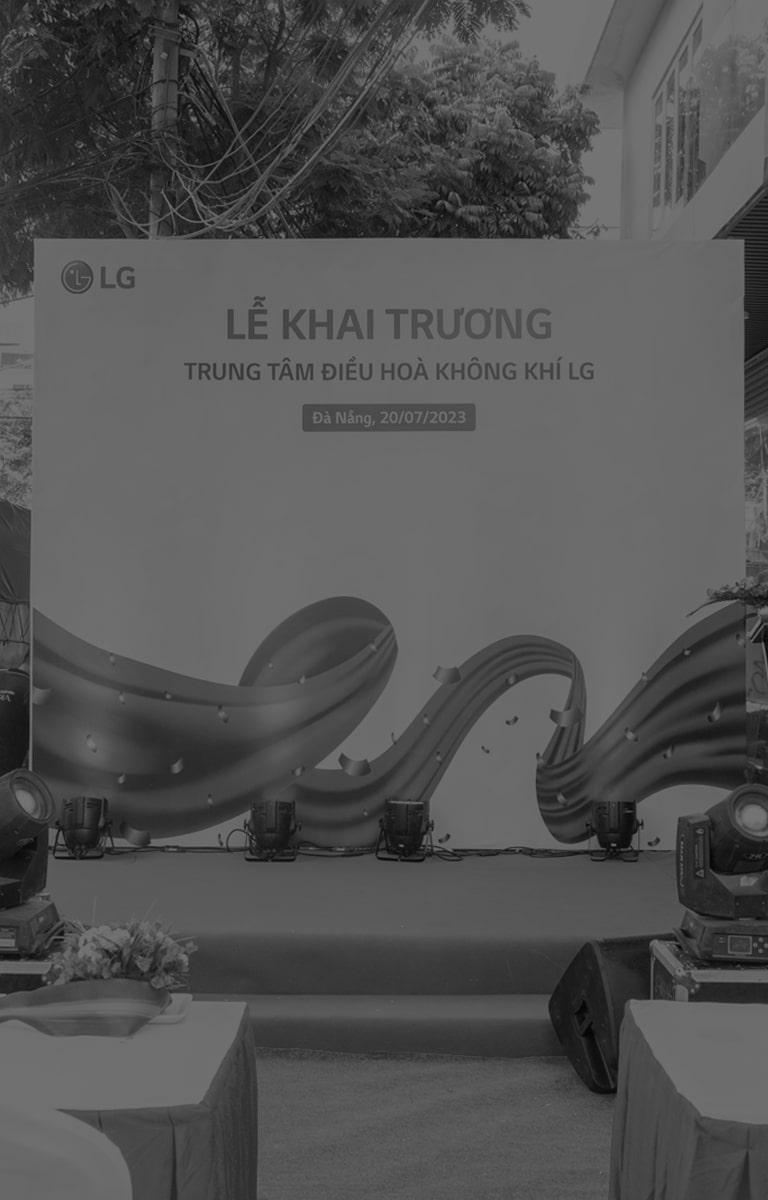 D??i t?m bi?n l?n 'H?c vi?n LG' ? góc trên bên trái, m?i ng??i ?ang ??ng thành nhi?u hàng trên b?c trong l? khai m?c. Bên trái h? là nh?ng bó hoa l?n màu ??.