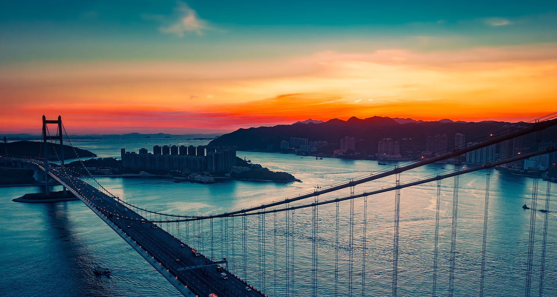En toda la pantalla aparece una vista aérea de una ciudad costera con tráfico circulando por un puente mientras se pone el sol. Se recorta y se muestra en una pantalla de televisión LG OLED con los colores originales sin cambios.
