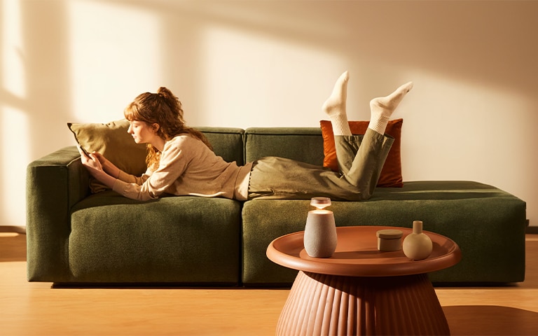 Frau genie?t auf dem Sofa den Klang der tragbaren, kabellosen Bluetooth-Lautsprecher LG XBOOM 360 mit 3-Wege-Surround-Sound-System