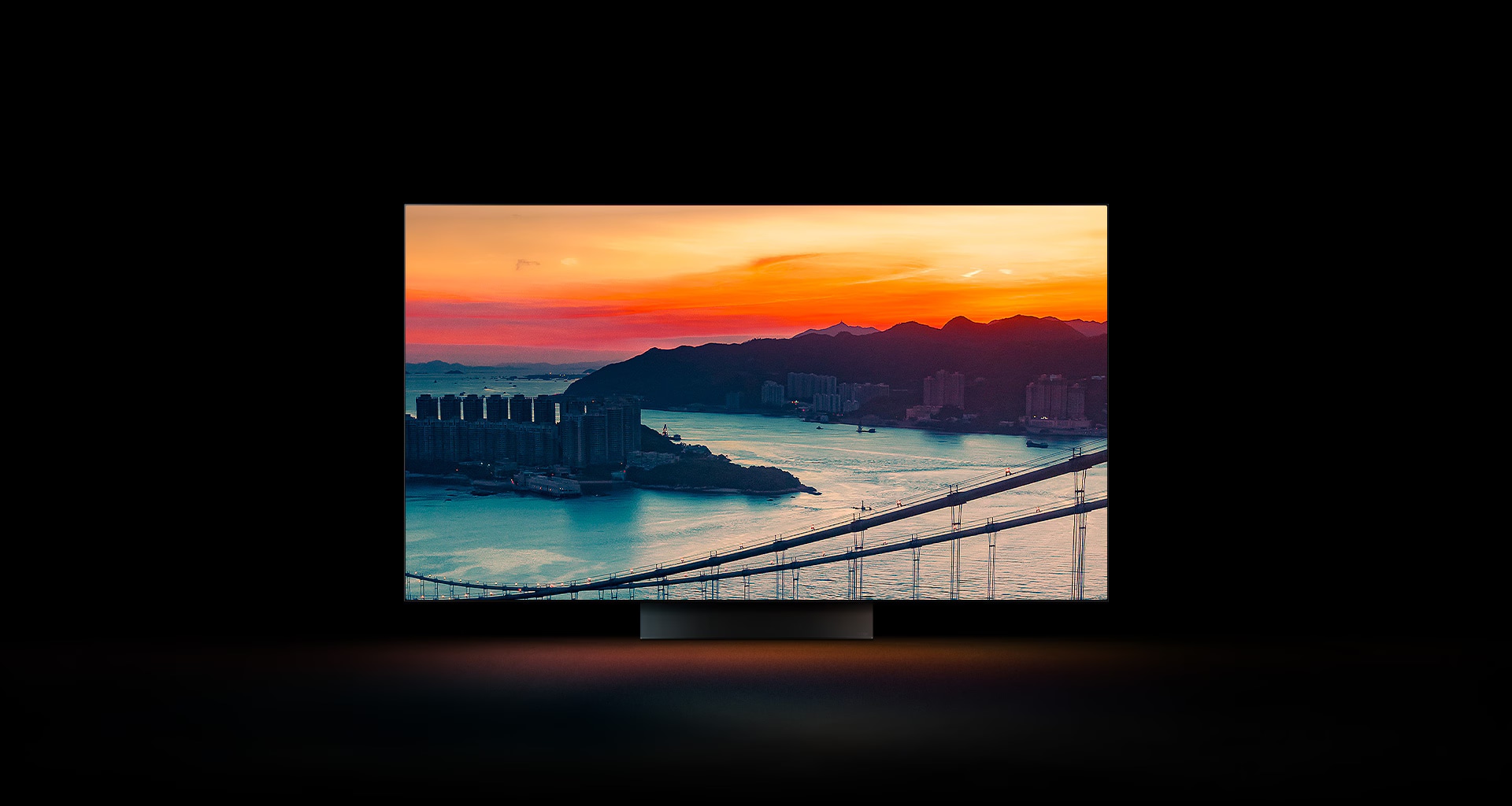 En vy ?ver en kuststad med trafik som k?r ?ver en bro medan solen g?r ner visas ?ver hela sk?rmen. Den ?r beskuren och visas p? en LG OLED-TV-sk?rm med de