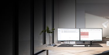 Ett modernt kontor med tv? datorsk?rmar p? ett skrivbord framf?r stora f?nster. Sk?rmarna visar kod och ett anv?ndargr?nssnitt. Kontoret ?r ljust inrett med v?xter, en skrivbordslampa och en kaffekopp. 