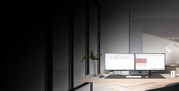 Ett modernt kontor med tv? datorsk?rmar p? ett skrivbord framf?r stora f?nster. Sk?rmarna visar kod och ett anv?ndargr?nssnitt. Kontoret ?r ljust inrett med v?xter, en skrivbordslampa och en kaffekopp. 