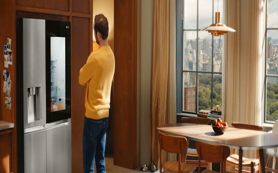 Mann in einem gelben Pullover bewundert einen LG-Kühlschrank und fragt sich womöglich ?Womit kann ich meinen Kühlschrank reinigen?” 
