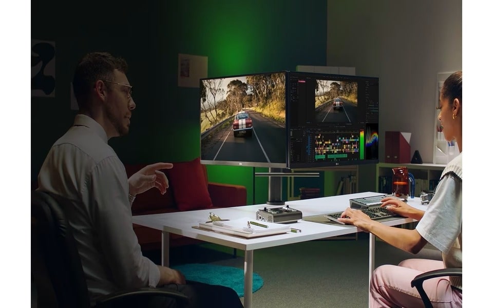Zwei Personen sitzen an einem Schreibtisch mit ihren eigenen Monitoren. Diese Monitore sind auf einer Seite verbunden, wodurch der Eindruck eines Doppelmonitors entsteht ? ein exemplarisches Multi-Monitor-Setup.