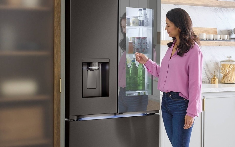 Eine Frau interagiert mit einem smarten InstaView®-Kühlschrank aus rostfreiem Stahl im ?Door-in-Door“-Design.
