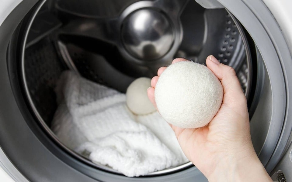 Das Innere eines energieeffizienten LG-Trockners mit der Nahaufnahme einer Person, die einen Wolltrocknerball in der Hand hält.