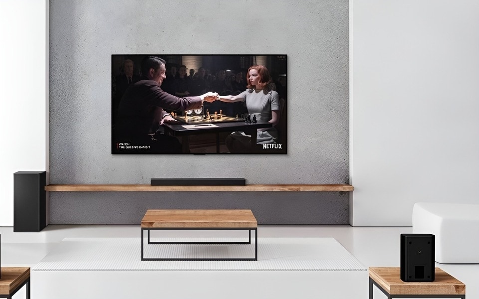 Ein minimalistisches Wohnzimmer mit einer Soundbar von LG und einem Subwoofer-Set unter einem an der Wand montierten Fernseher. Die für dich beste TV Soundbar von LG lässt dich die Netflix-Serie noch spannender verfolgen. 