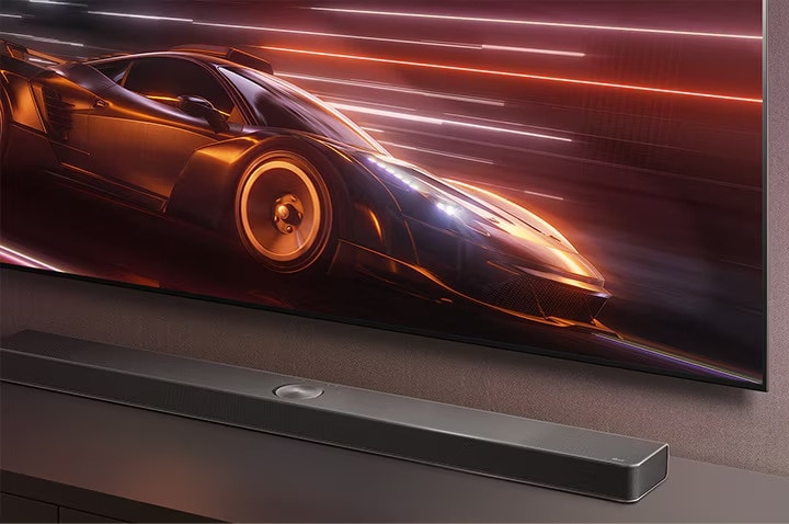 Nahaufnahme einer top Soundbar von LG, die sich auf einer TV-Konsole befindet. Der Fernsehbildschirm darüber zeigt ein dynamisches Rennspiel, was dank der Soundbar das Gaming-Erlebnis intensiviert.