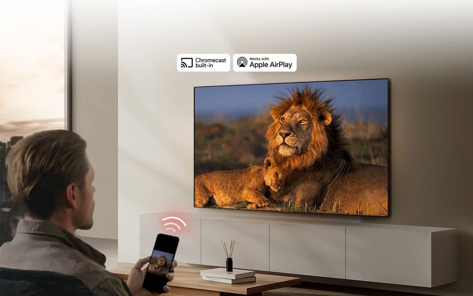 Eine Person streamt ein Bild von einem Löwen auf einen modernen LG Smart-TV, mit eingebauten Funktionen für Chromecast und Apple AirPlay.