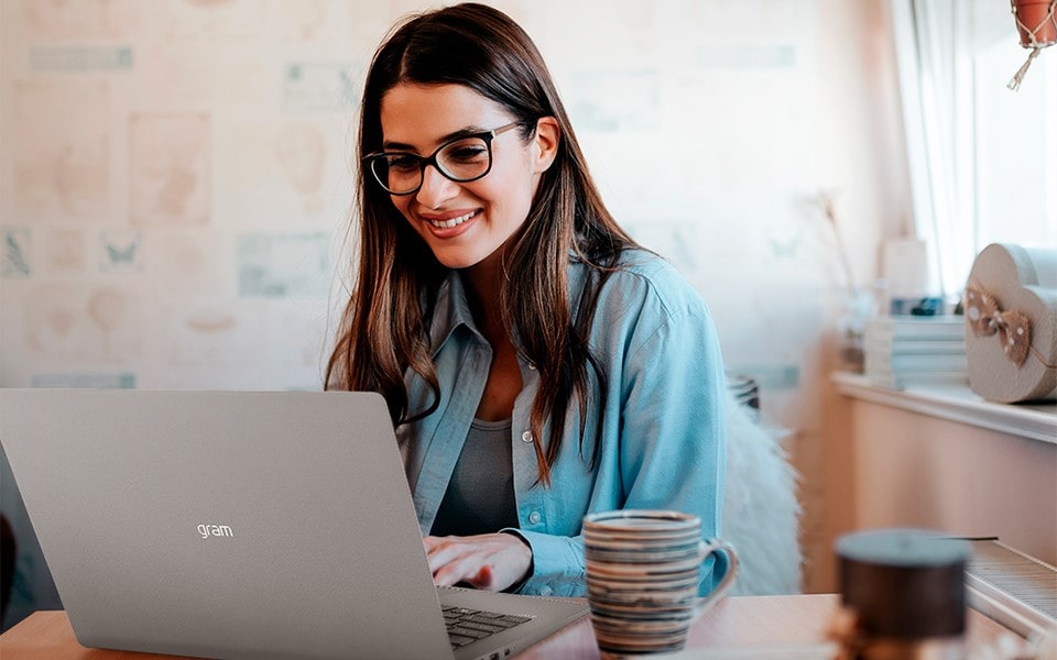 Eine Frau mit Brille arbeitet an einem Tisch auf ihrem Laptop
