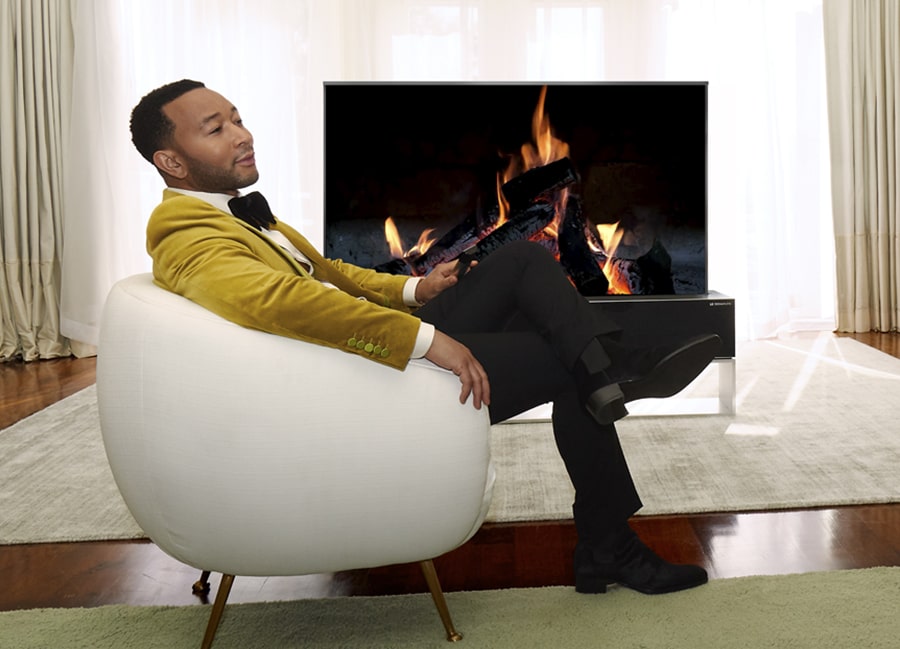 John Legend sitzt in einem wei?en Stuhl vor einem aufrollbaren OLED-Fernseher von LG SIGNATURE.