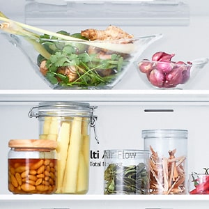 Close up view of lg bottom freezer refrigerator shelf with various fresh herbs, vegetables, and preserved foods in glass containers.
