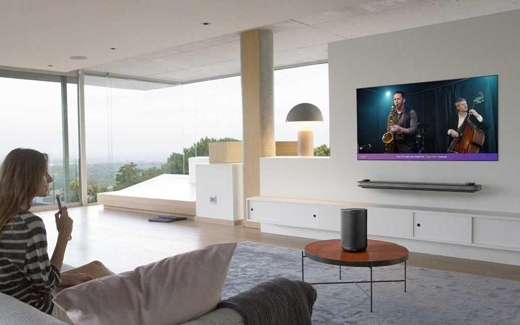 Una mujer sentada en su salón, usando el mando a distancia para hablar con su televisor LG OLED.