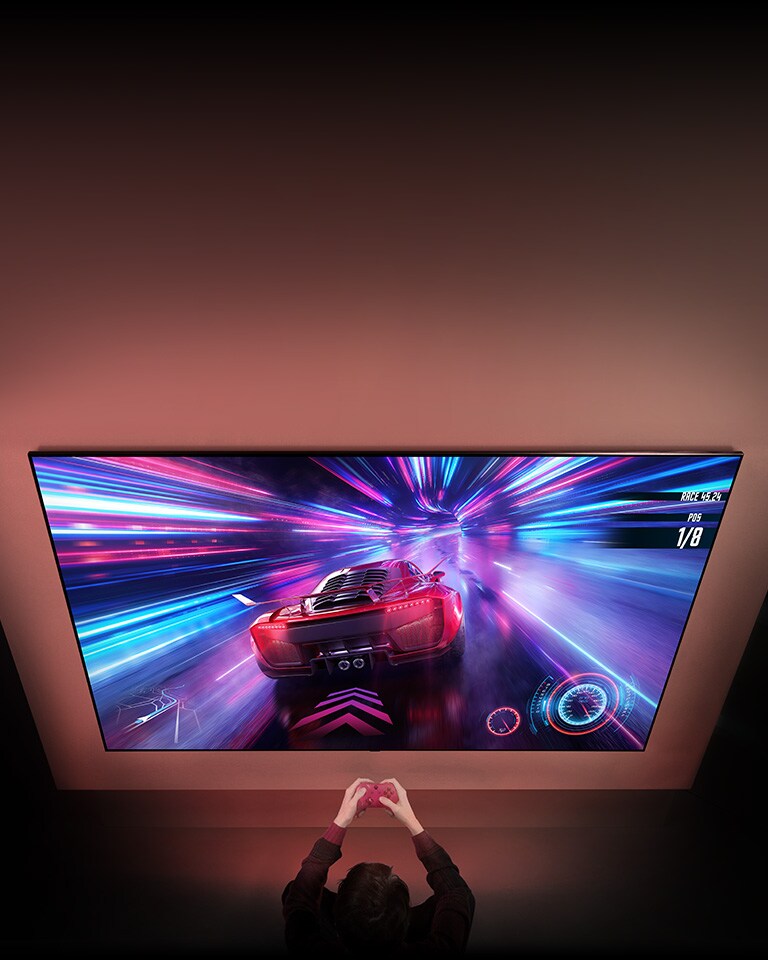 Suuri televisio on sein?ll?, ja n?yt?ll? n?kyy k?ynniss? oleva autopeli. Television edess? peliohjain n?kyy peliin keskittyneen henkil?n k?siss?.
