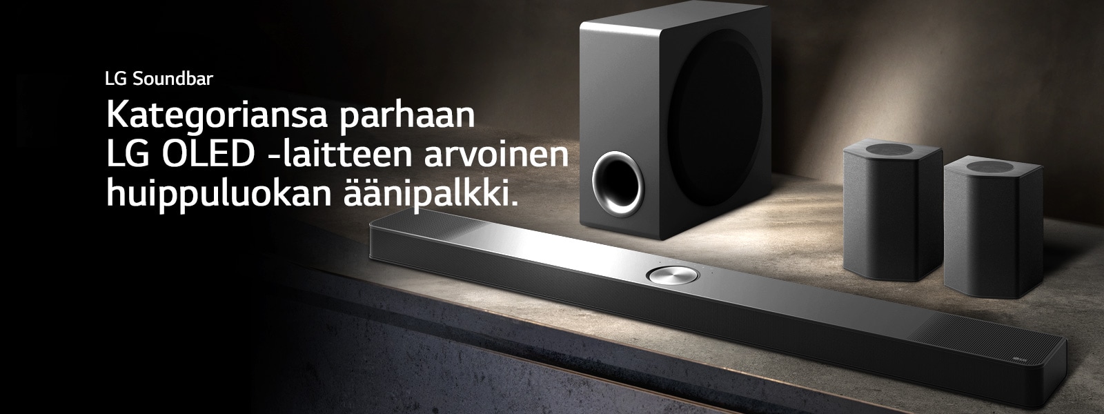 LG Soundbar, takakaiuttimet ja subwoofer on asetettu kulmasta n?kyv??n ruskeaan puuhyllyyn mustassa huoneessa, jonka ainoa valaistus kohdistuu ??nij?rjestelm??n.