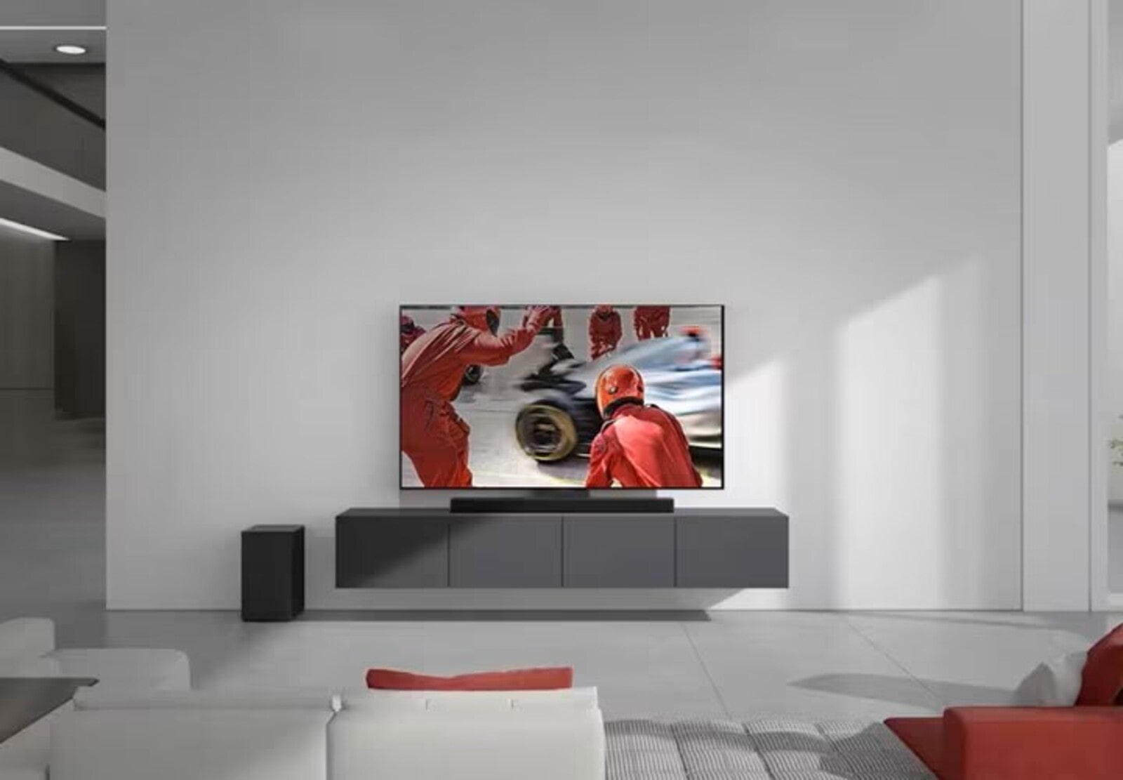 Salon moderne avec une télévision murale affichant une scène de course automobile, avec une barre de son en dessous et un caisson de basse sur le côté. Un canapé blanc et rouge est placé en face de la télévision.