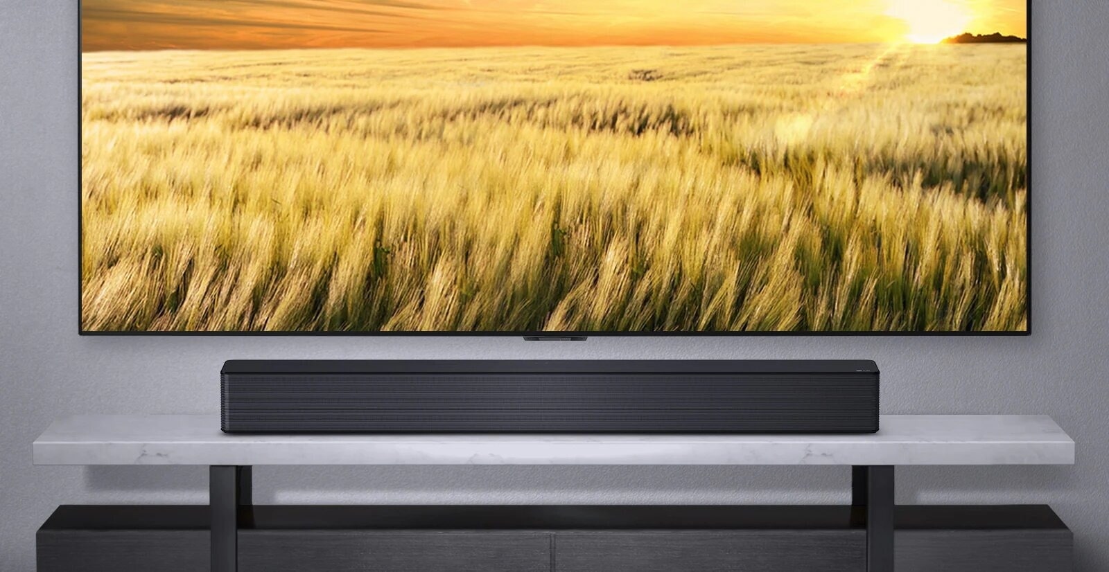 Une barre de son LG placée sous un téléviseur grand écran affichant un paisible champ de blé aux couleurs dorées. L’élégant meuble TV en marbre complète le design épuré de la barre de son.