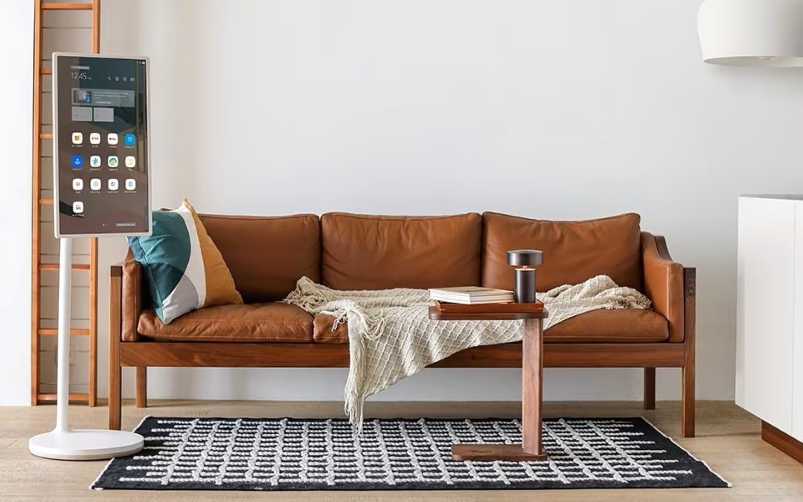 Un salon cosy avec un canapé en cuir marron, un écran numérique sur un support, une petite table basse en bois et un tapis à motifs, créant une atmosphère chaleureuse et accueillante.