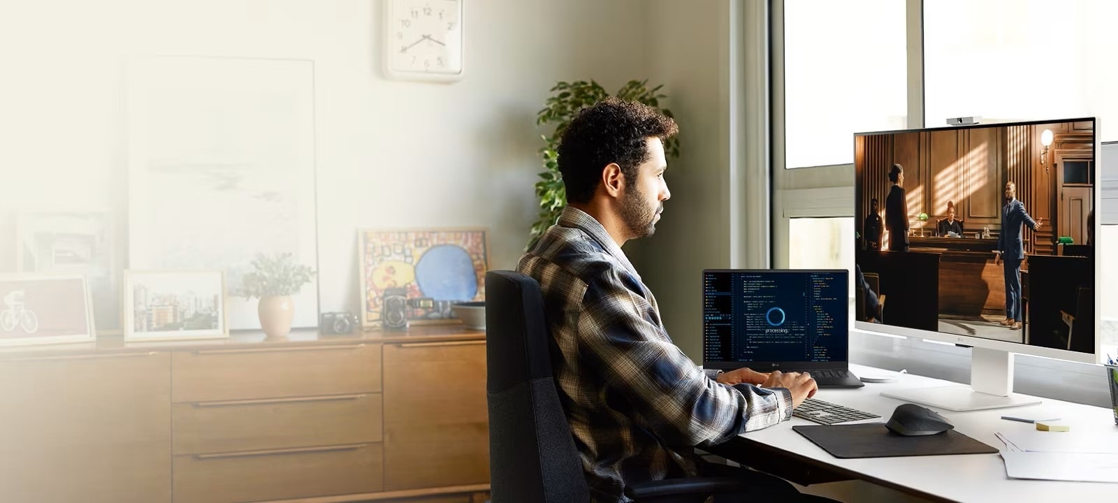 personne travaillant à un bureau avec un moniteur LG et un ordinateur portable. Le moniteur affiche une scène d’une vidéo ou d’un film, tandis que l’ordinateur portable affiche du code ou des données. L’espace de travail est lumineux et organisé, avec des plantes, des ?uvres d’art et une fenêtre qui apporte de la lumière naturelle.