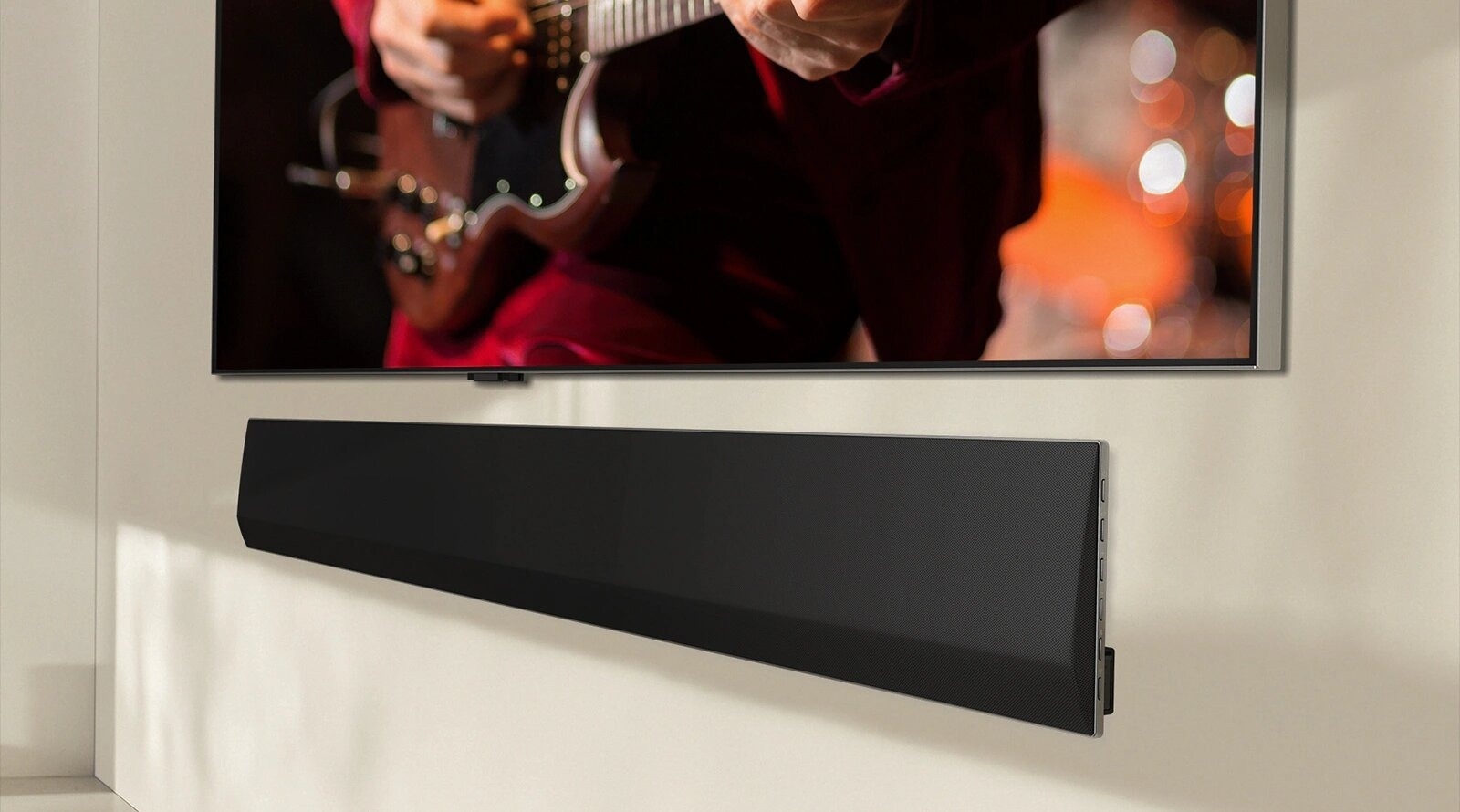 Une barre de son LG sous un écran de télévision montrant une personne jouant de la guitare électrique. La focalisation se fait sur les mains et la guitare, avec un arrière-plan flou aux couleurs chaudes, créant une atmosphère chaleureuse. L’installation présente un système de divertissement de haute qualité.