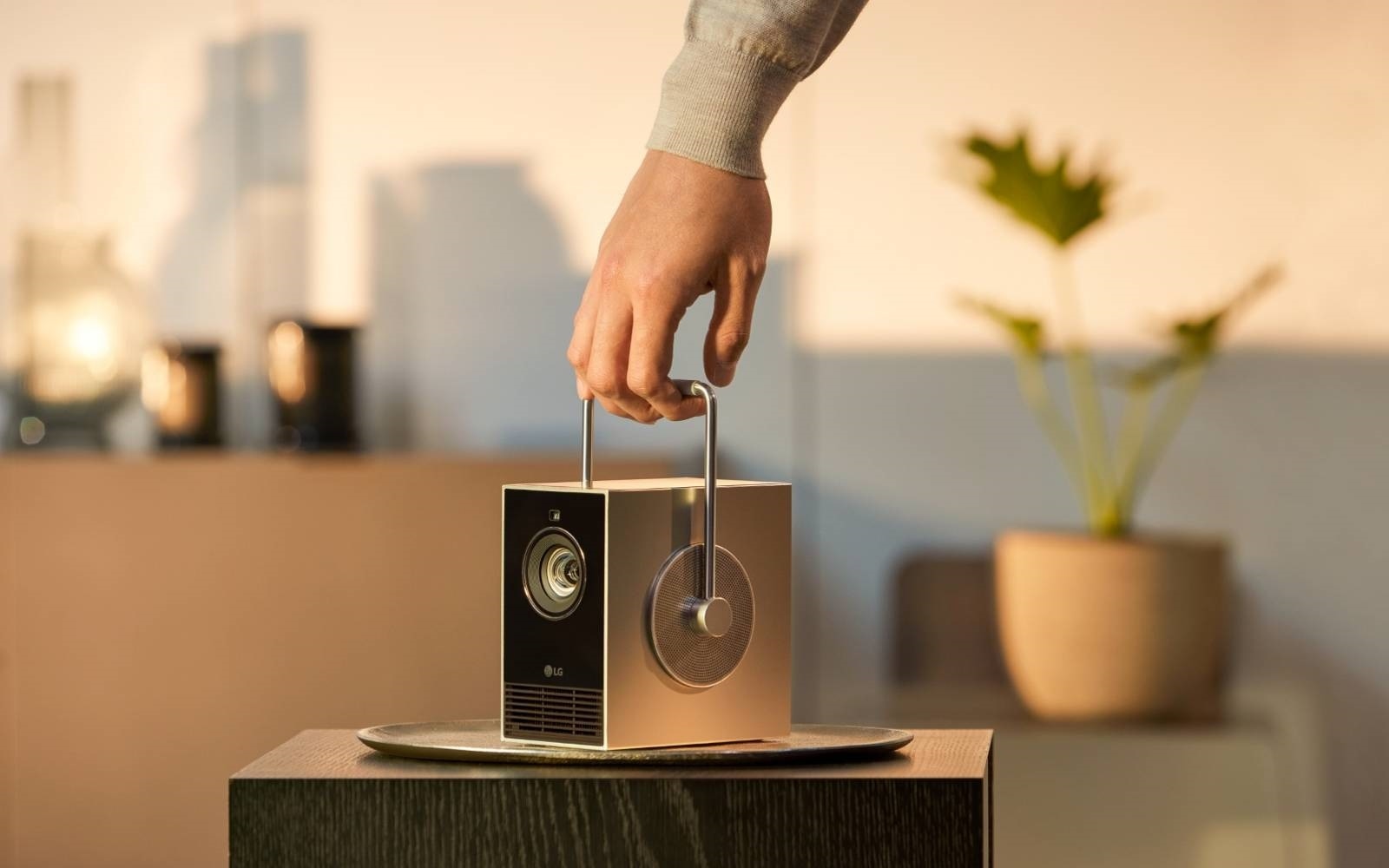 Une personne porte un projecteur compact et élégant avec une poignée intégrée, prête à être installé facilement. La scène se déroule dans une pièce faiblement éclairée, avec un décor moderne et des éléments de design minimalistes.