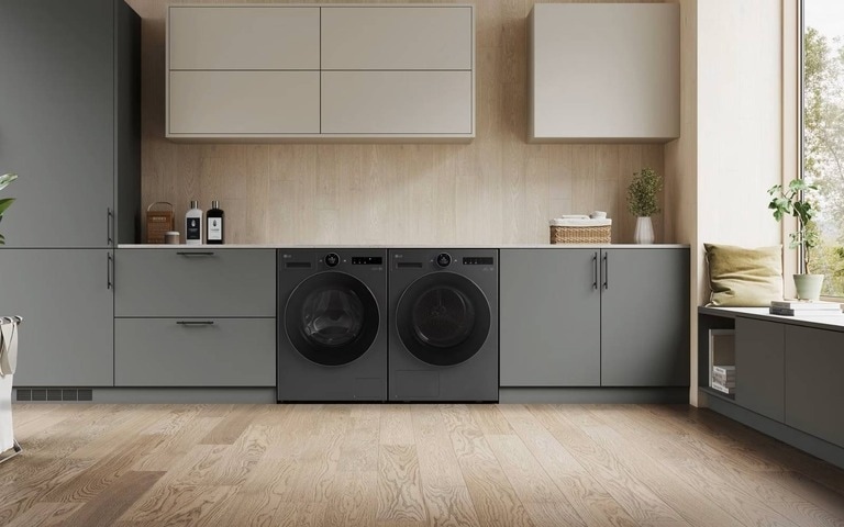 Une buanderie élégante avec des unités de lave-linge et sèche-linge noires assorties intégrées dans des armoires grises, des accents en bois clair et une grande fenêtre laissant entrer la lumière naturelle.