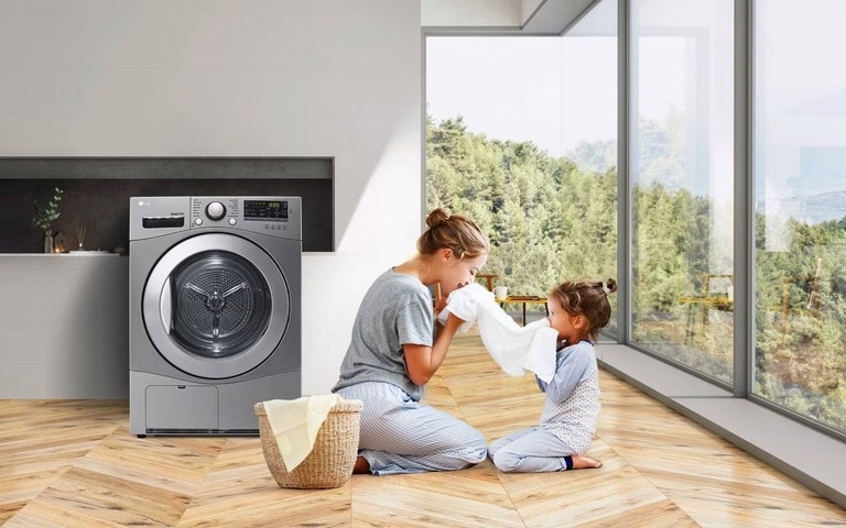Une mère et sa fille sentent le linge frais sorti de la machine à laver LG dans une pièce claire et lumineuse, soulignant l’entretien en douceur des tissus.