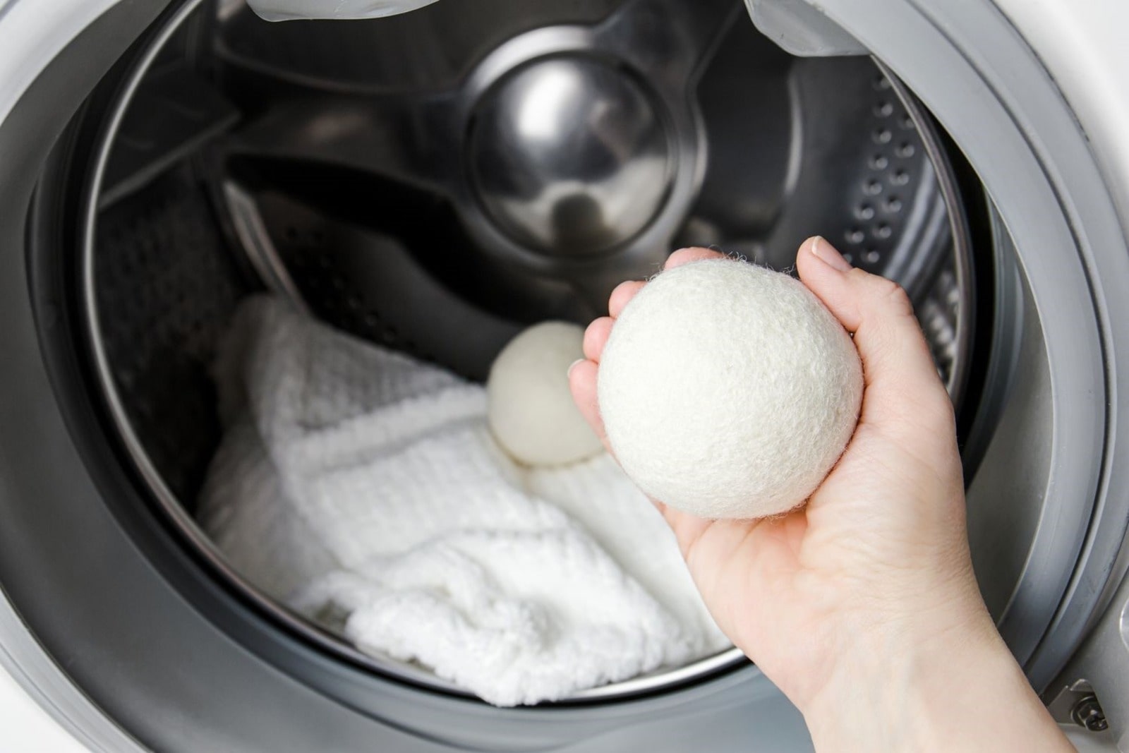 L’intérieur d’un lave-linge ou sèche-linge LG avec une personne tenant une boule de laine dans la main. Une serviette blanche et une autre boule de séchage se trouvent à l’intérieur du tambour, démontrant l’utilisation d’alternatives écologiques pour la lessive.