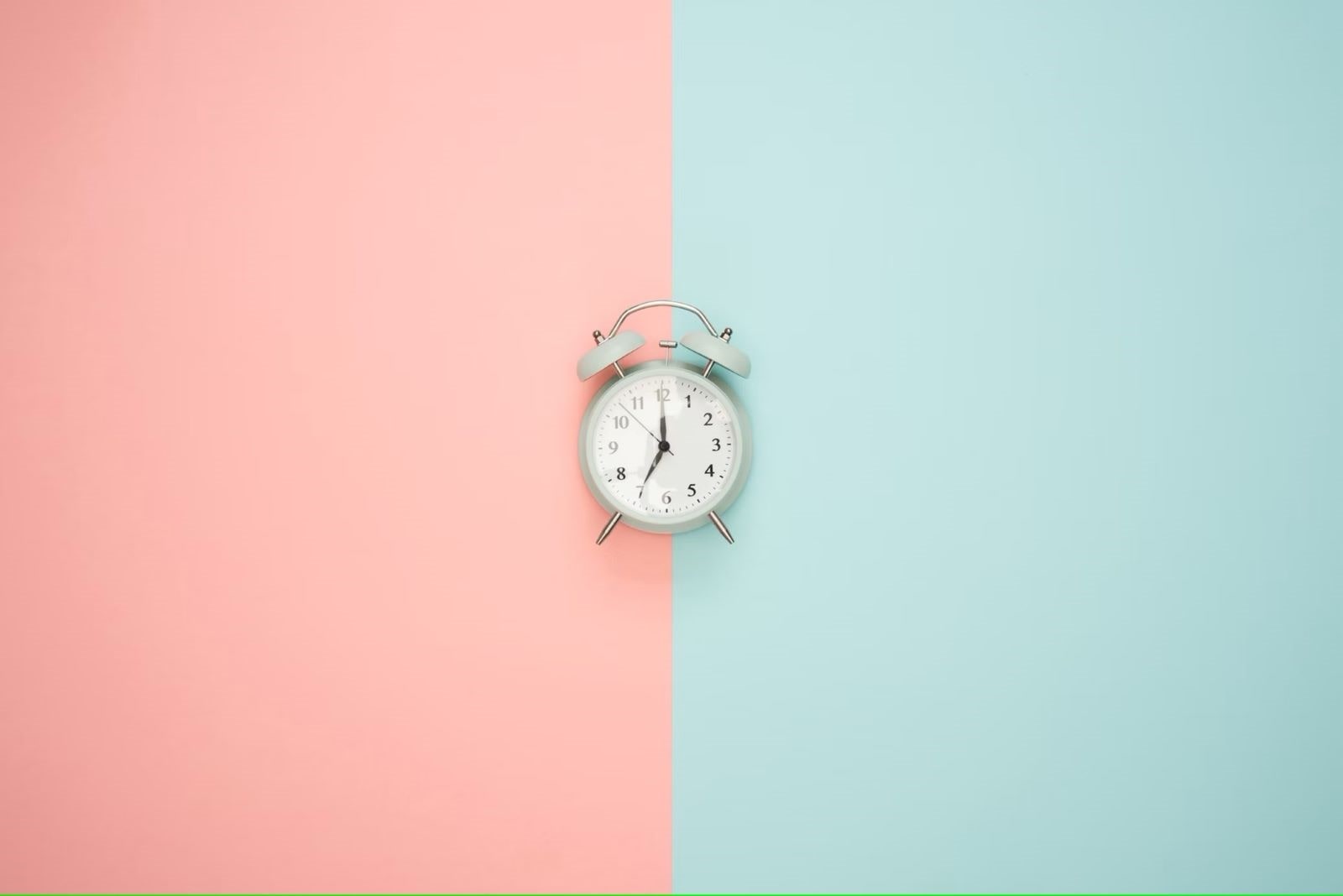 Réveil blanc avec des aiguilles noires placé au centre d'un fond bicolore, rose à gauche et bleu clair à droite.