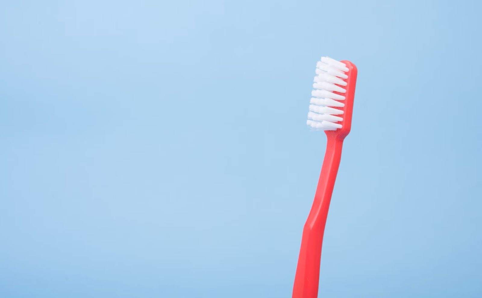 Brosse à dents rouge avec des poils blancs sur un fond bleu clair, symbolisant la propreté et l'entretien, tout comme les techniques de nettoyage pour frigo en inox et pour enlever les mauvaises odeurs du frigo.