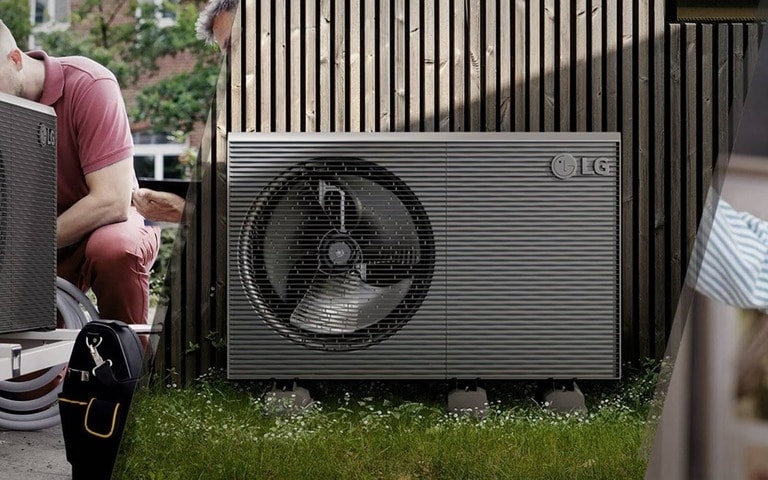 Un technicien travaillant sur un système de pompe à chaleur LG à l'extérieur, avec l'unité installée contre un mur en bois, mettant en avant l'entretien et l'installation.