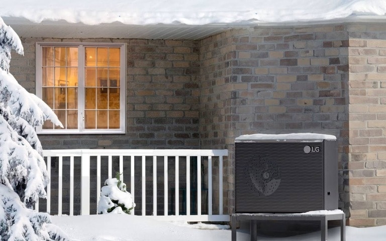 Un système de pompe à chaleur LG en fonctionnement dans un environnement enneigé, à l'extérieur d'une maison en briques, mettant en avant l'efficacité et la fiabilité de l'unité dans des conditions hivernales.