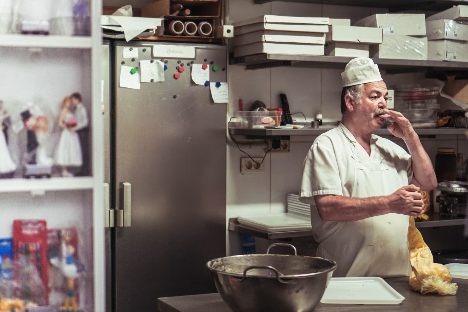 Un pâtissier dans une cuisine professionnelle, avec un réfrigérateur en inox en arrière-plan, illustrant l'histoire et l'évolution des réfrigérateurs.